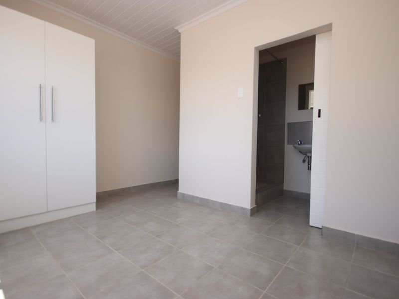 A clean, empty bedroom featuring neutral tiled flooring, a built-in wardrobe, and direct access to an en-suite bathroom.
