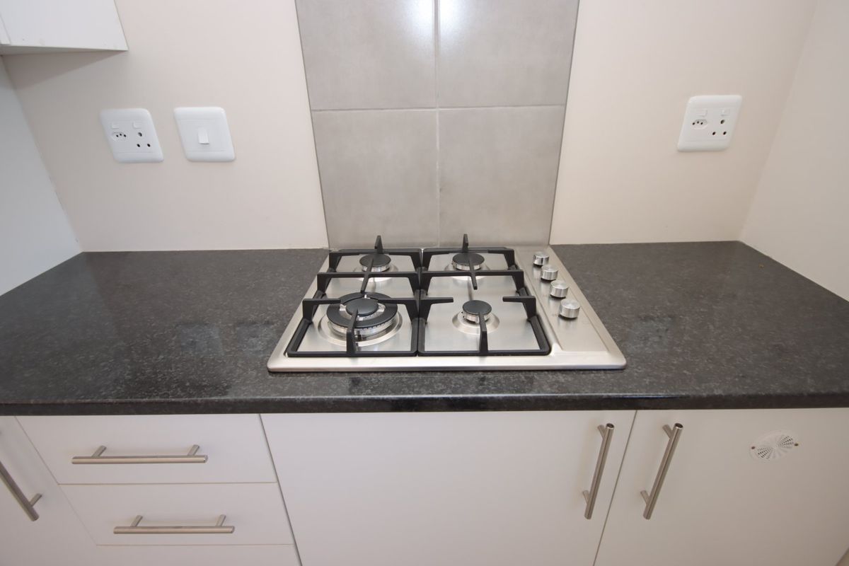 A clean, modern kitchen area featuring a stainless steel gas hob set into a dark granite countertop with neutral cabinetry and tiled splashback.
