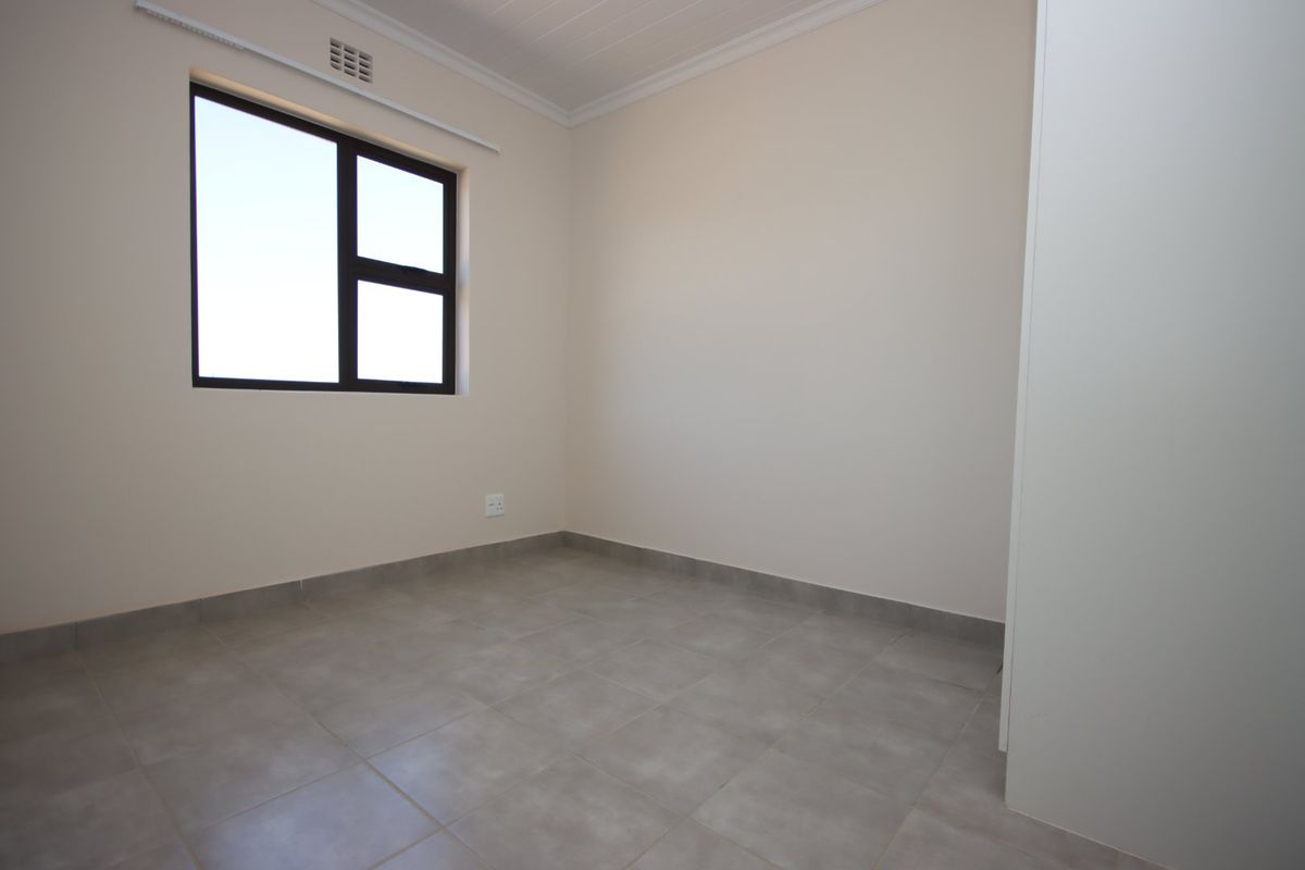 A clean, empty bedroom featuring neutral tiled flooring, a built-in cupboard, and a modern aluminium window frame.