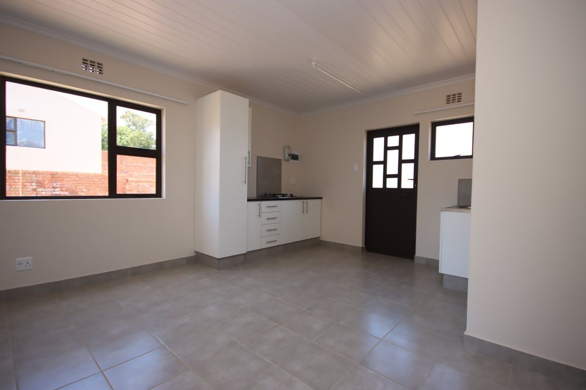 A clean, empty kitchen featuring tiled flooring, built-in cabinetry with a gas hob, and direct access to the exterior.