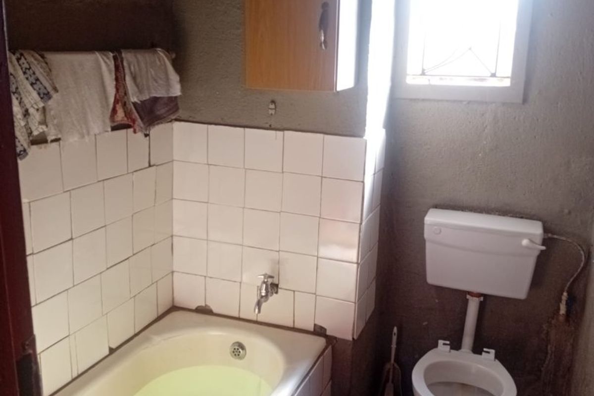 A compact bathroom featuring a bathtub, toilet, and wall-mounted cabinet, requiring significant renovation to improve finishes and overall condition.