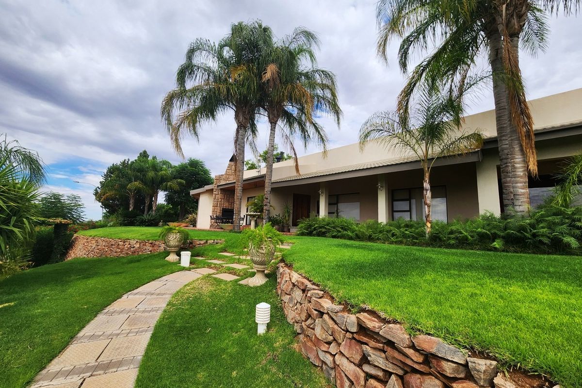 A well-maintained rear garden featuring a stone retaining wall, paved pathway, and a covered patio area with an integrated outdoor fireplace.