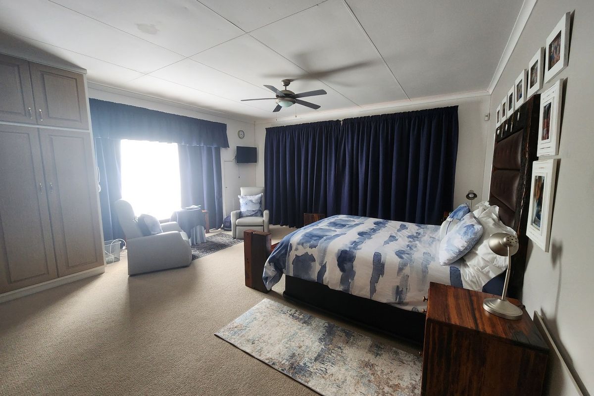 Spacious bedroom featuring built-in cupboards, a ceiling fan, and neutral carpeting. The room offers ample space for a seating area.