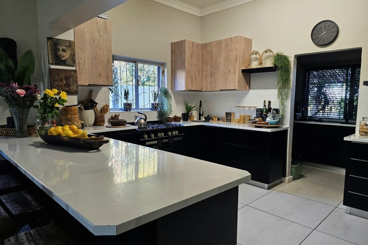 Modern kitchen featuring a central island with quartz countertops, sleek black lower cabinetry, light wood upper cabinets, and a gas stove.