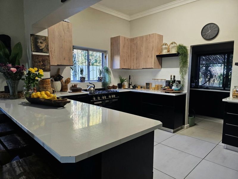 Modern kitchen featuring a central island with quartz countertops, sleek black lower cabinetry, light wood upper cabinets, and a gas stove.