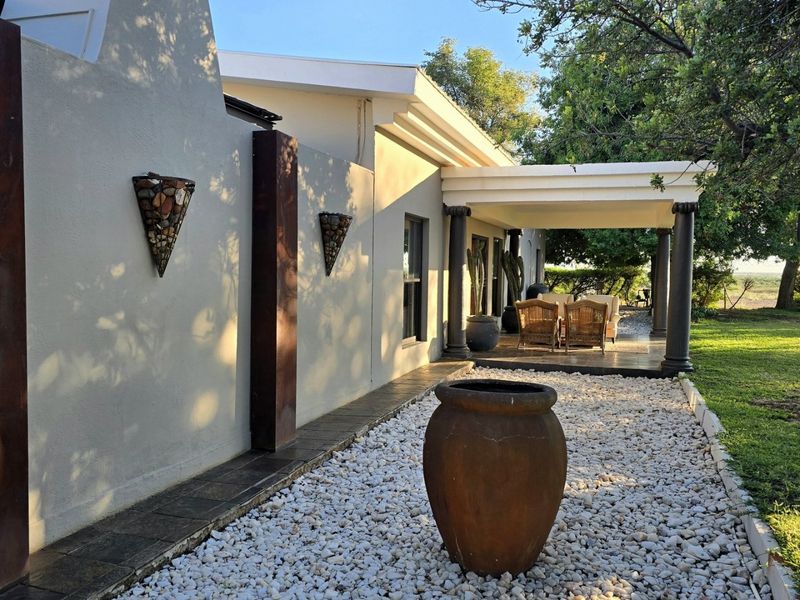 A well-maintained covered patio area featuring stone-tiled flooring and decorative columns, overlooking a landscaped garden with a gravel pathway.