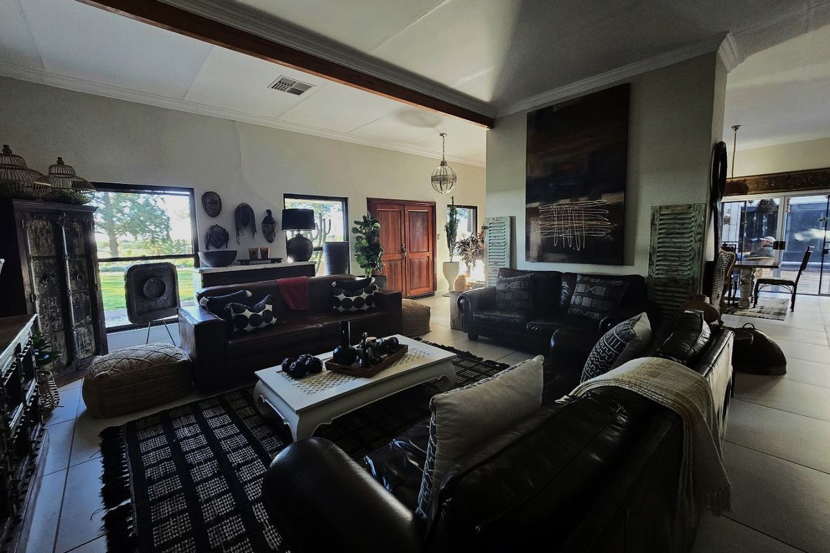 Spacious living area featuring tiled flooring, an exposed timber ceiling beam, and large windows providing natural light and garden views.