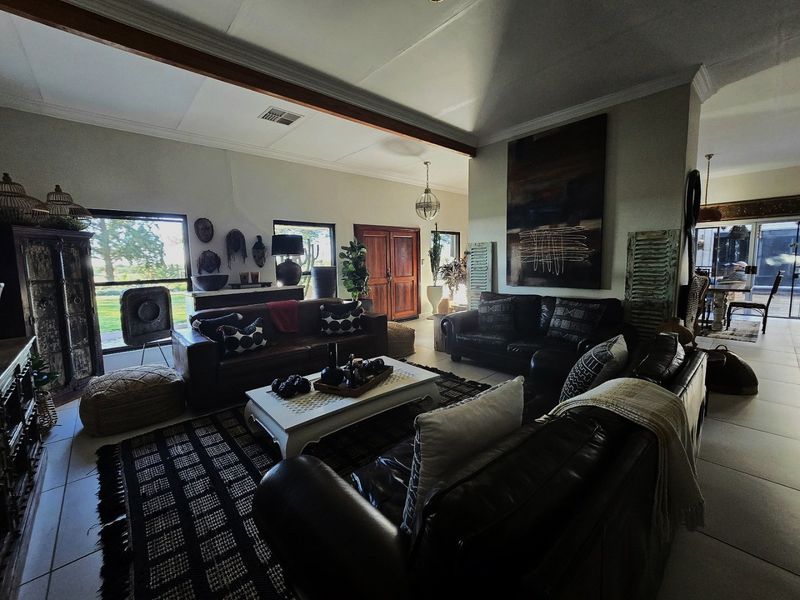 Spacious living area featuring tiled flooring, an exposed timber ceiling beam, and large windows providing natural light and garden views.
