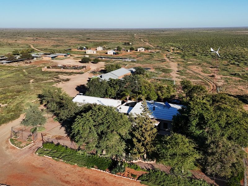 Aerial view of a rural farm property featuring a main residence, multiple outbuildings, surrounding landscape, and a wind turbine.