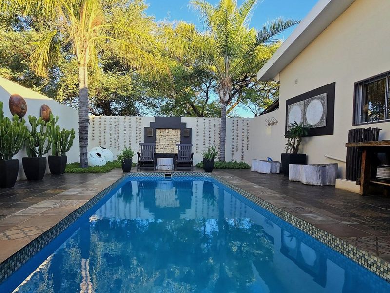A well-maintained outdoor pool area featuring a tiled surround, boundary wall, and integrated water feature, set within a private garden space.
