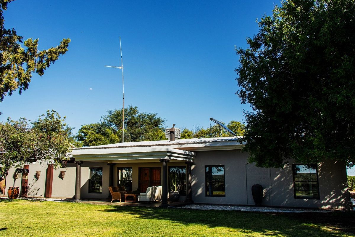 Rear view of the farm property featuring a covered patio, metal roofing, and integrated solar water heating system set within a spacious garden.