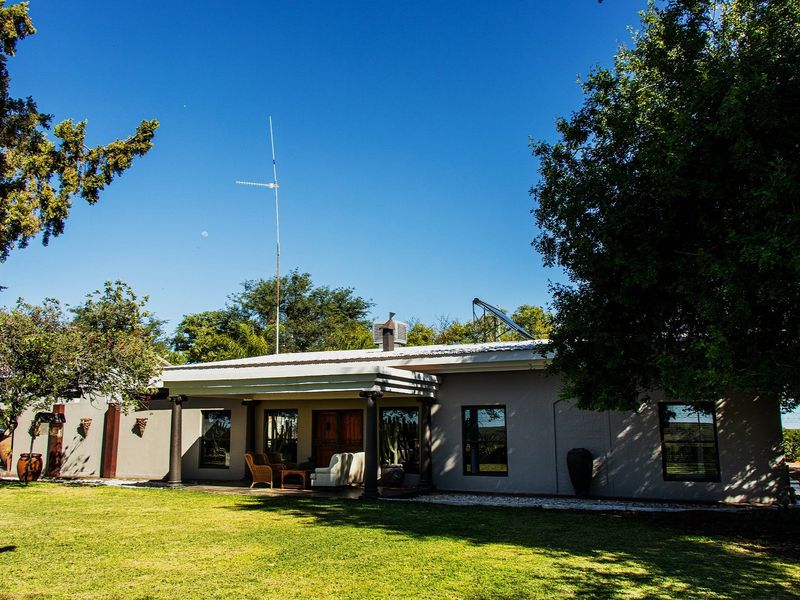 Rear view of the farm property featuring a covered patio, metal roofing, and integrated solar water heating system set within a spacious garden.