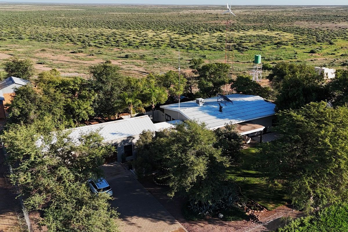 Aerial view of a farm property featuring a main dwelling with a metal roof, wind turbine, water tank, and expansive surrounding landscape.
