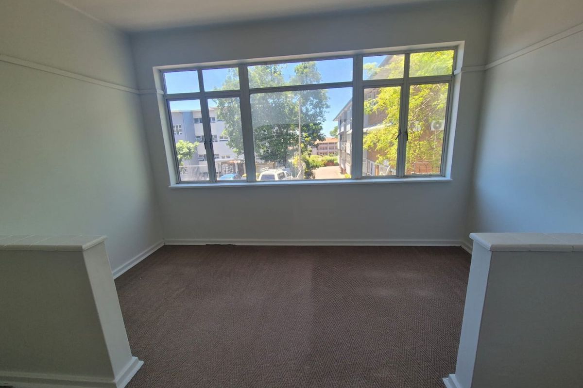 A bright, empty living area featuring large windows, carpeted flooring, and classic picture rails, offering a blank canvas for interior design.