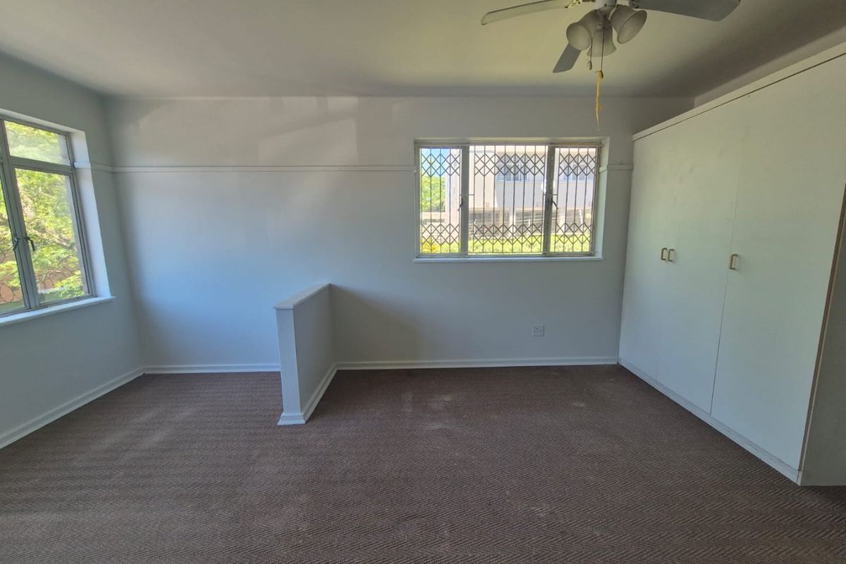 Spacious bedroom featuring built-in cupboards, a ceiling fan, and security bars on the windows, offering a blank canvas for personalization.