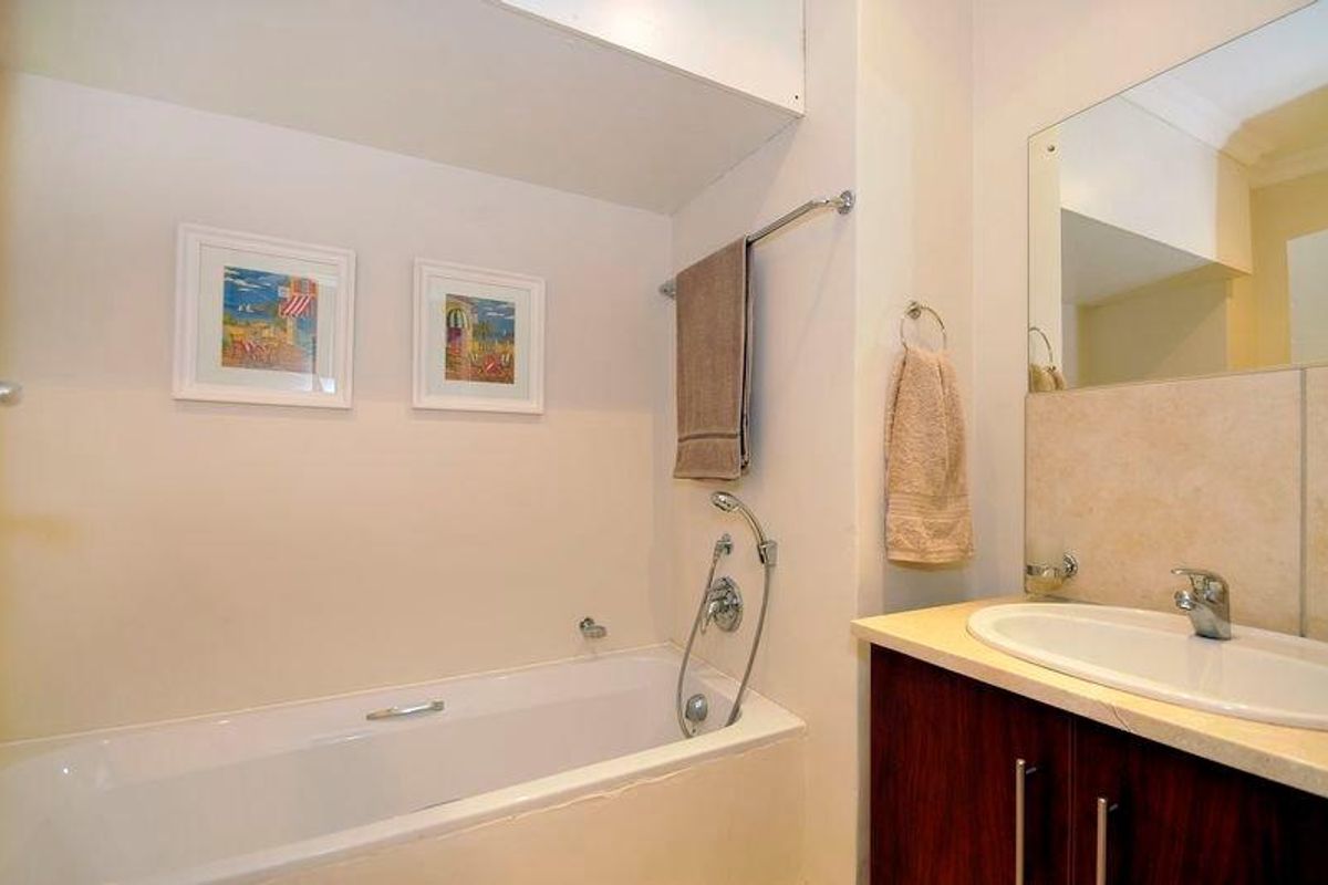A functional bathroom featuring a built-in bathtub with shower mixer, a vanity cabinet with an integrated basin, and a wall-mounted mirror.