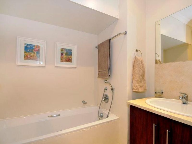 A functional bathroom featuring a built-in bathtub with shower mixer, a vanity cabinet with an integrated basin, and a wall-mounted mirror.