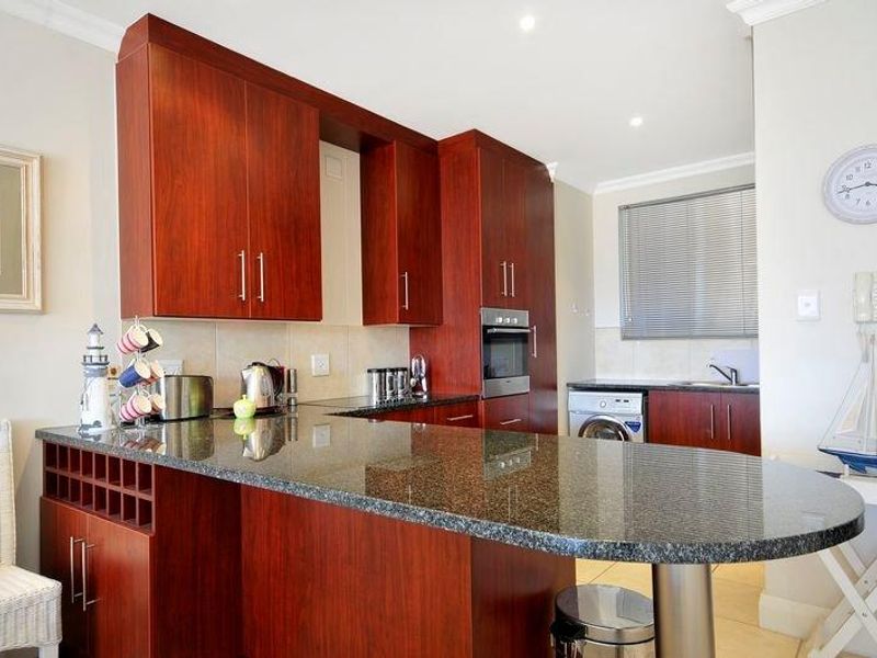 A functional kitchen featuring dark wood cabinetry, granite countertops, a breakfast bar, built-in oven, and integrated laundry appliance space.