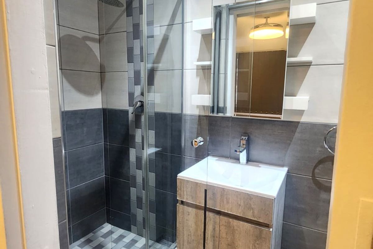 Modern bathroom featuring a glass-enclosed shower with a rain shower head, a vanity cabinet with basin, and a mirrored medicine cabinet.