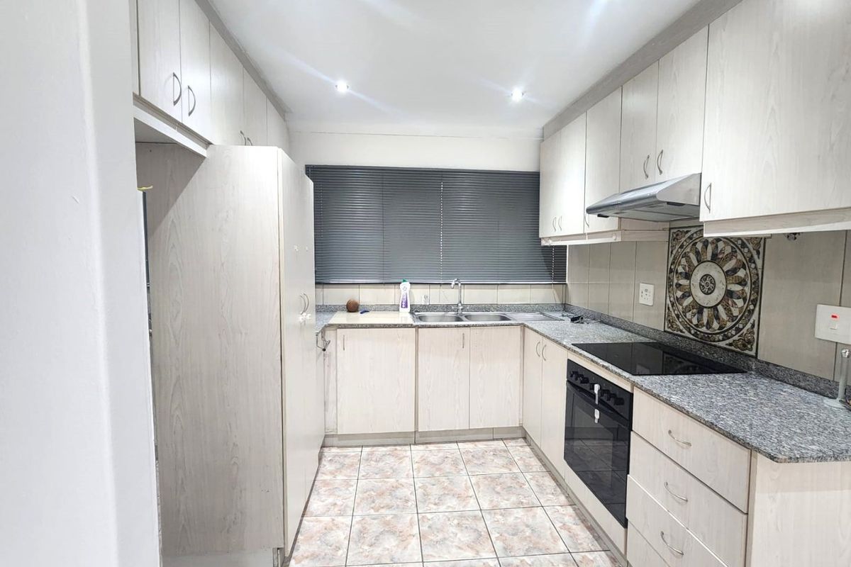 A functional kitchen featuring light wood-finish cabinetry, granite countertops, integrated oven and hob, and tiled flooring with ample storage space.