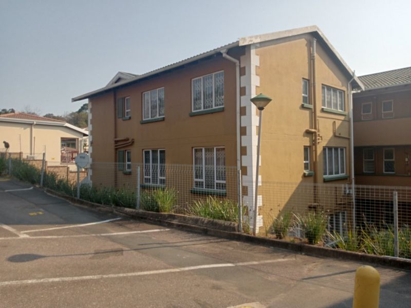 Exterior view of a two-story apartment building featuring a mustard-colored facade, tiled roof, and security bars on the windows.