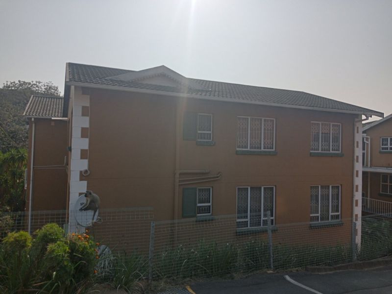 A view of the rear elevation of a multi-story apartment building featuring tiled roofing, security bars on windows, and perimeter mesh fencing.