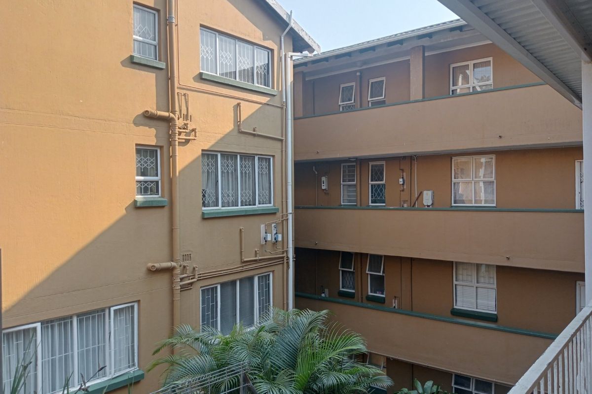 View of the apartment complex exterior, showing multiple levels with security bars on windows and external plumbing infrastructure.