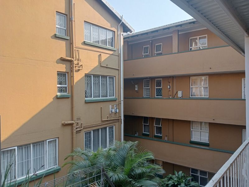 View of the apartment complex exterior, showing multiple levels with security bars on windows and external plumbing infrastructure.