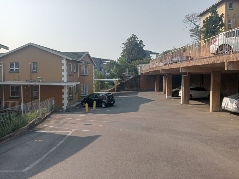 Exterior view of the apartment complex showing the parking area, concrete support structures, and building facade.