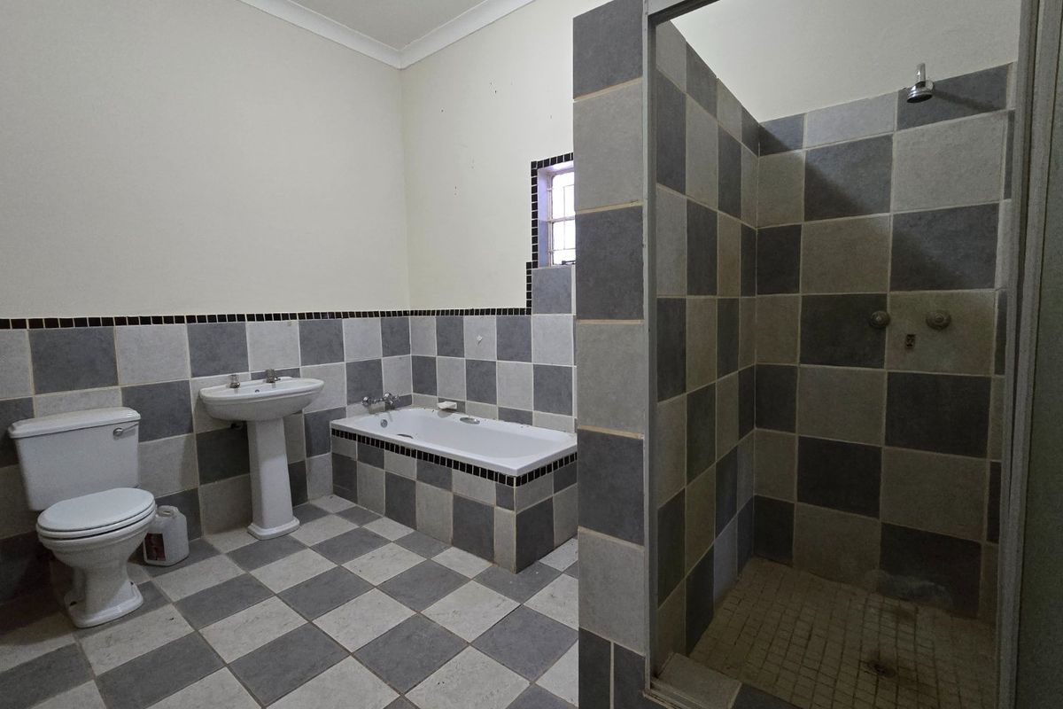 A spacious bathroom featuring a walk-in shower, built-in bathtub, and pedestal basin with a classic grey and white checkered tile finish.