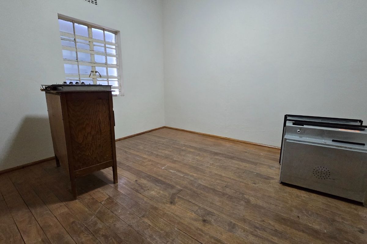 An empty bedroom featuring original timber flooring, a window with security bars, and neutral wall finishes, offering a blank canvas for renovation.
