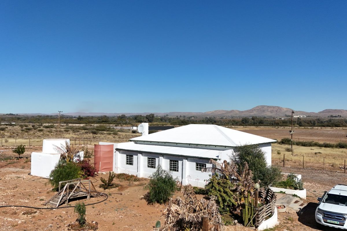 Aerial view of a farmhouse with a white corrugated metal roof, set in a rural landscape with surrounding water storage tanks and fencing.