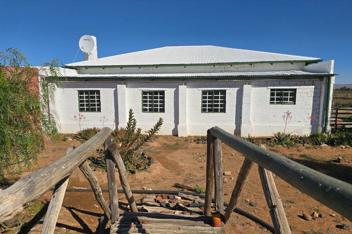Rear view of a white masonry farm building with a corrugated metal roof, featuring a rustic wooden footbridge in the foreground.