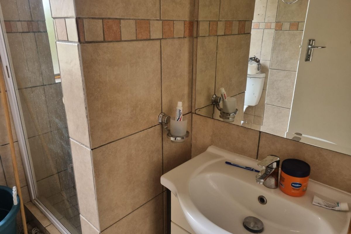 A functional bathroom featuring a vanity basin with a mixer tap, a wall-mounted mirror, and a separate shower enclosure with tiled walls.