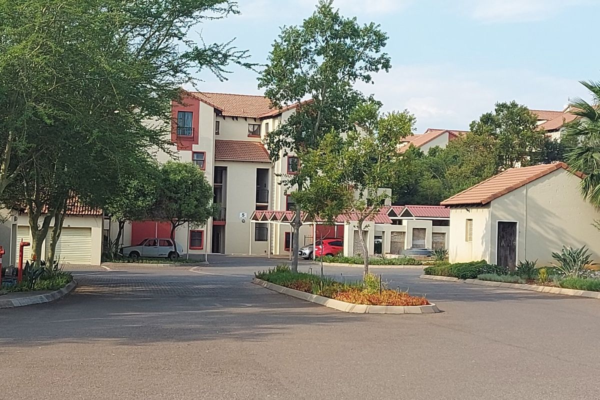 Exterior view of an apartment complex featuring paved driveways, covered parking, and established landscaped garden beds.
