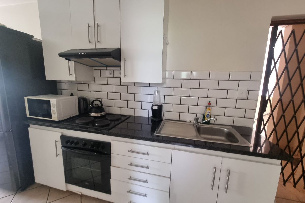 Modern kitchen featuring white cabinetry, black granite countertops, subway tile backsplash, and integrated appliances including an oven and hob.