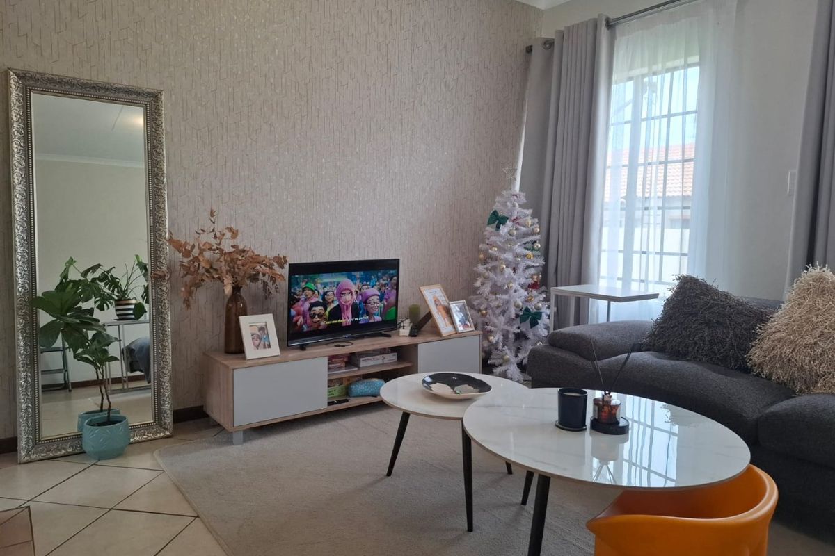 A well-maintained living room featuring tiled flooring, textured wallpaper, and large windows with curtain tracks, offering a comfortable and inviting living space.