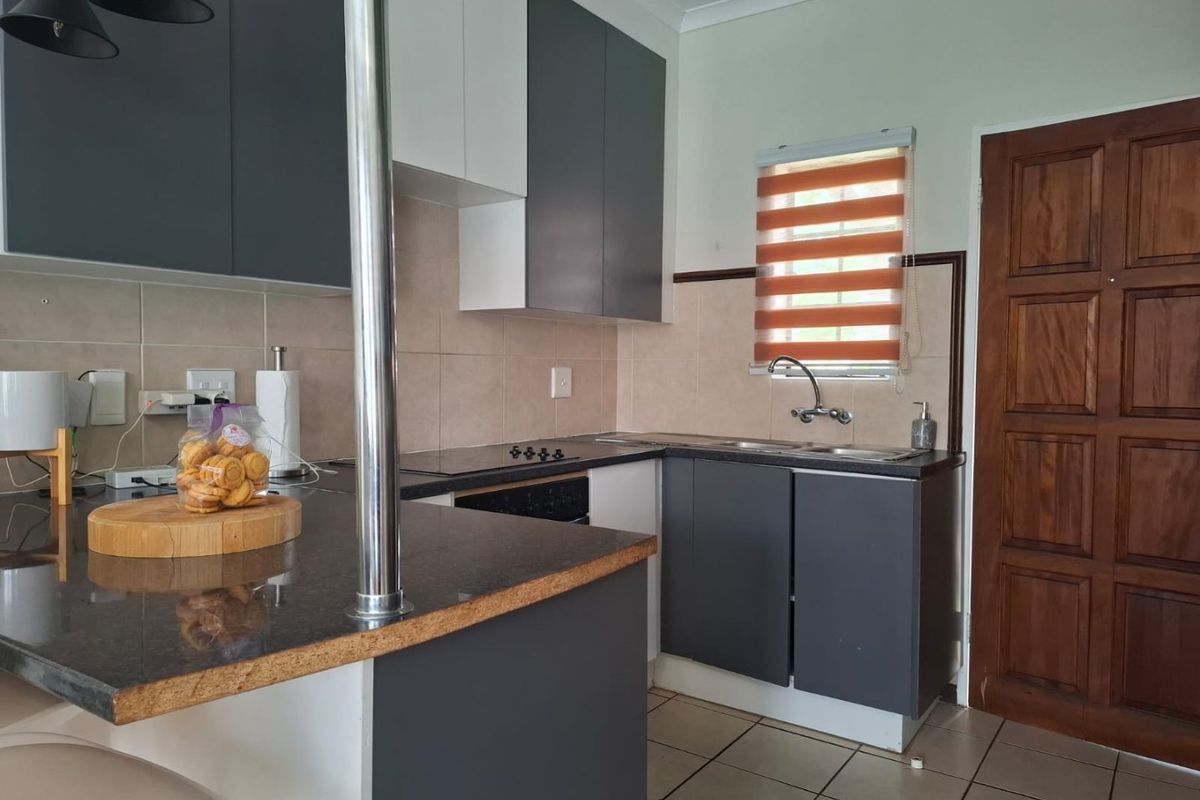 A functional kitchen featuring modern two-tone cabinetry, granite countertops, a built-in hob and oven, and tiled flooring with a practical layout.