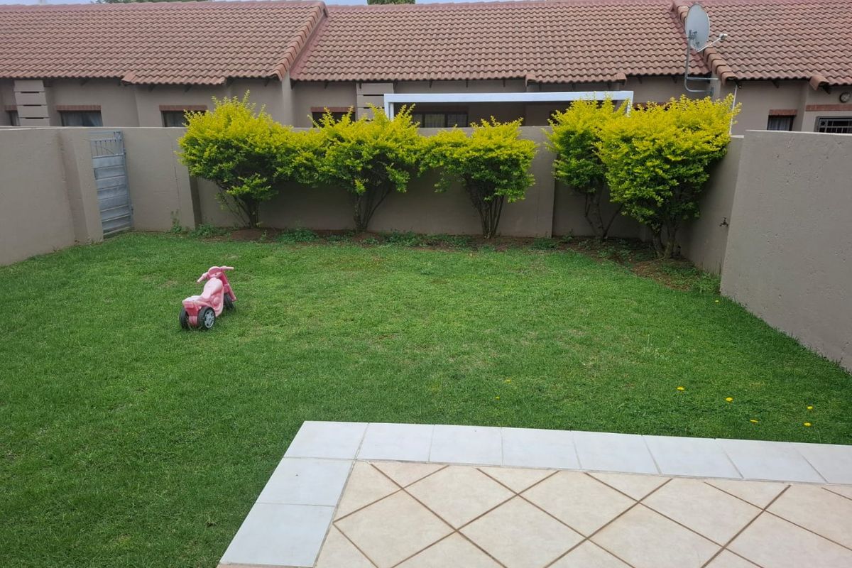 A private rear garden featuring a tiled patio area, well-maintained lawn, and perimeter walling, providing a functional outdoor space for the townhouse.