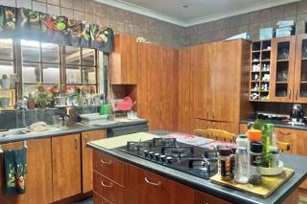 A functional kitchen featuring extensive wooden cabinetry, a central island with a built-in gas hob, and a tiled backsplash.