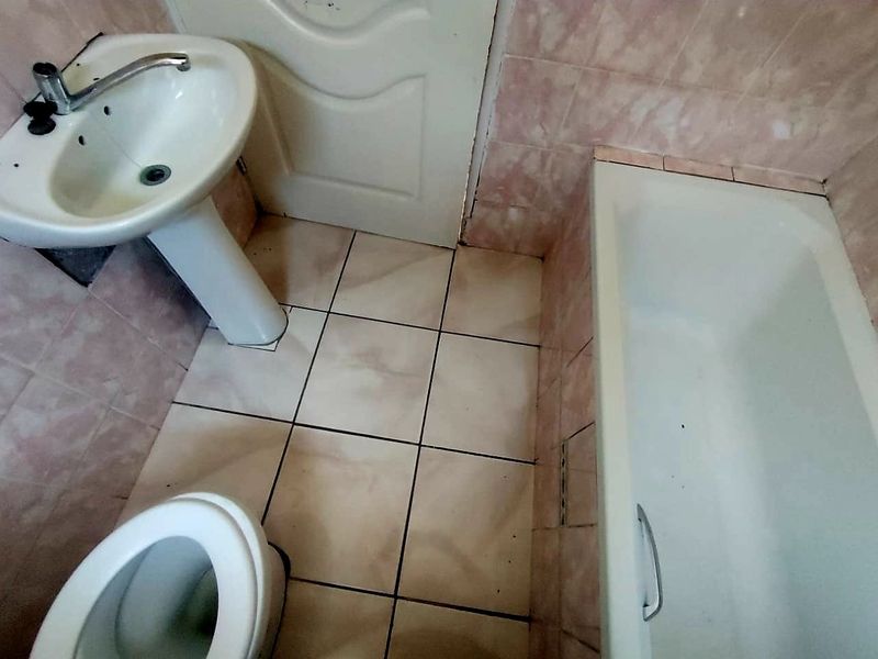 A dated bathroom featuring a pedestal basin, bathtub, and toilet with worn ceramic tiling throughout, requiring renovation to modernize the space.