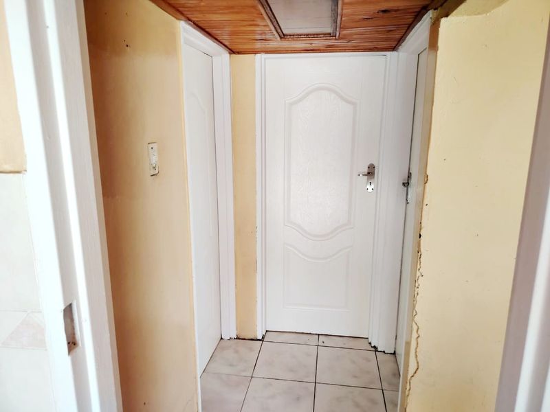 A narrow hallway featuring tiled flooring and a timber ceiling, showing signs of wear and requiring cosmetic updates to the walls and finishes.