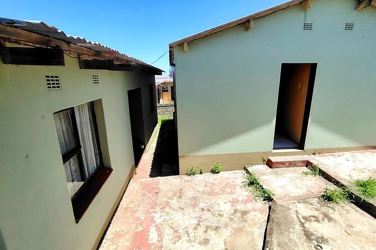 Exterior view of the rear of the property showing two structures with concrete paving and visible wear on the exterior finishes.