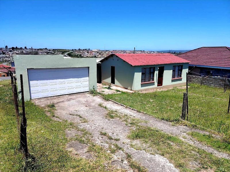 Front view of a detached house featuring a single garage, concrete driveway, and a corrugated metal roof, set on a grassed plot.