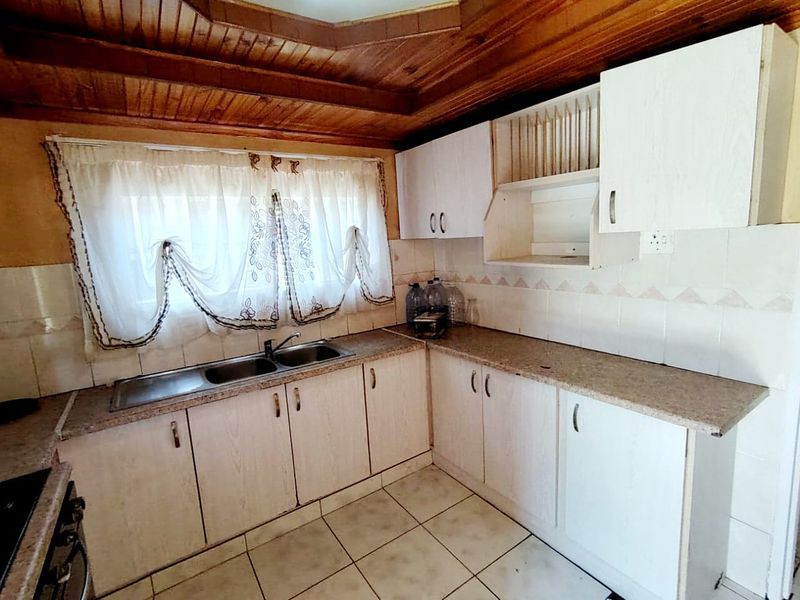 A dated kitchen featuring laminate cabinetry, a double bowl stainless steel sink, tiled splashbacks, and a timber tongue and groove ceiling.