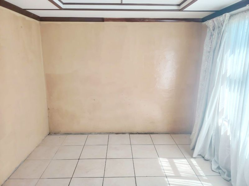 An empty bedroom featuring tiled flooring and timber ceiling trim, requiring cosmetic updates to the wall finishes.