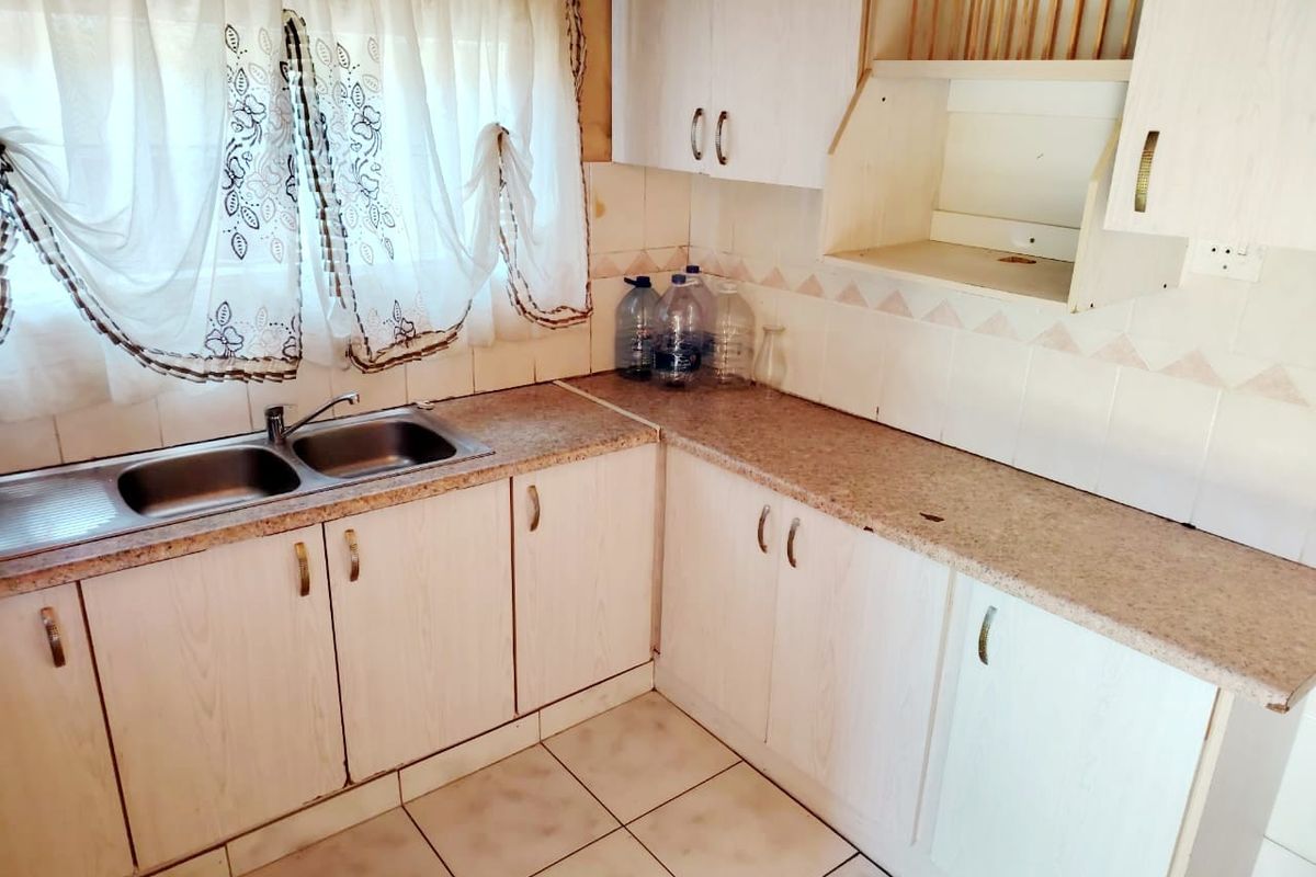 A dated kitchen featuring laminate countertops, built-in cabinetry, and a double bowl stainless steel sink, offering potential for modernization and renovation.