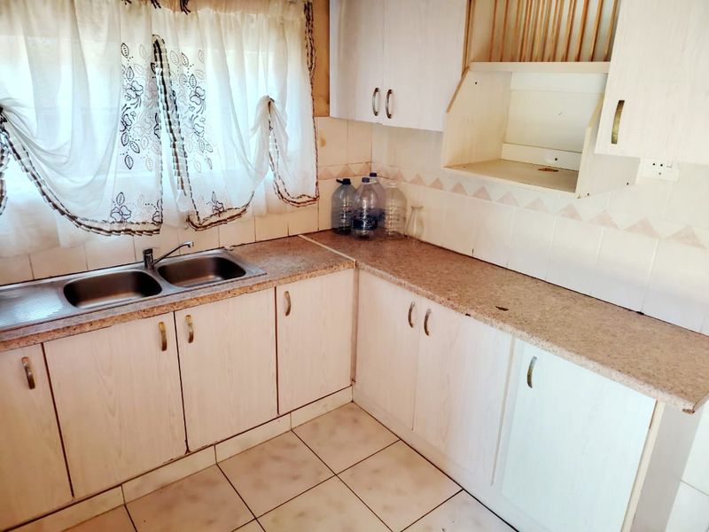 A dated kitchen featuring laminate countertops, built-in cabinetry, and a double bowl stainless steel sink, offering potential for modernization and renovation.
