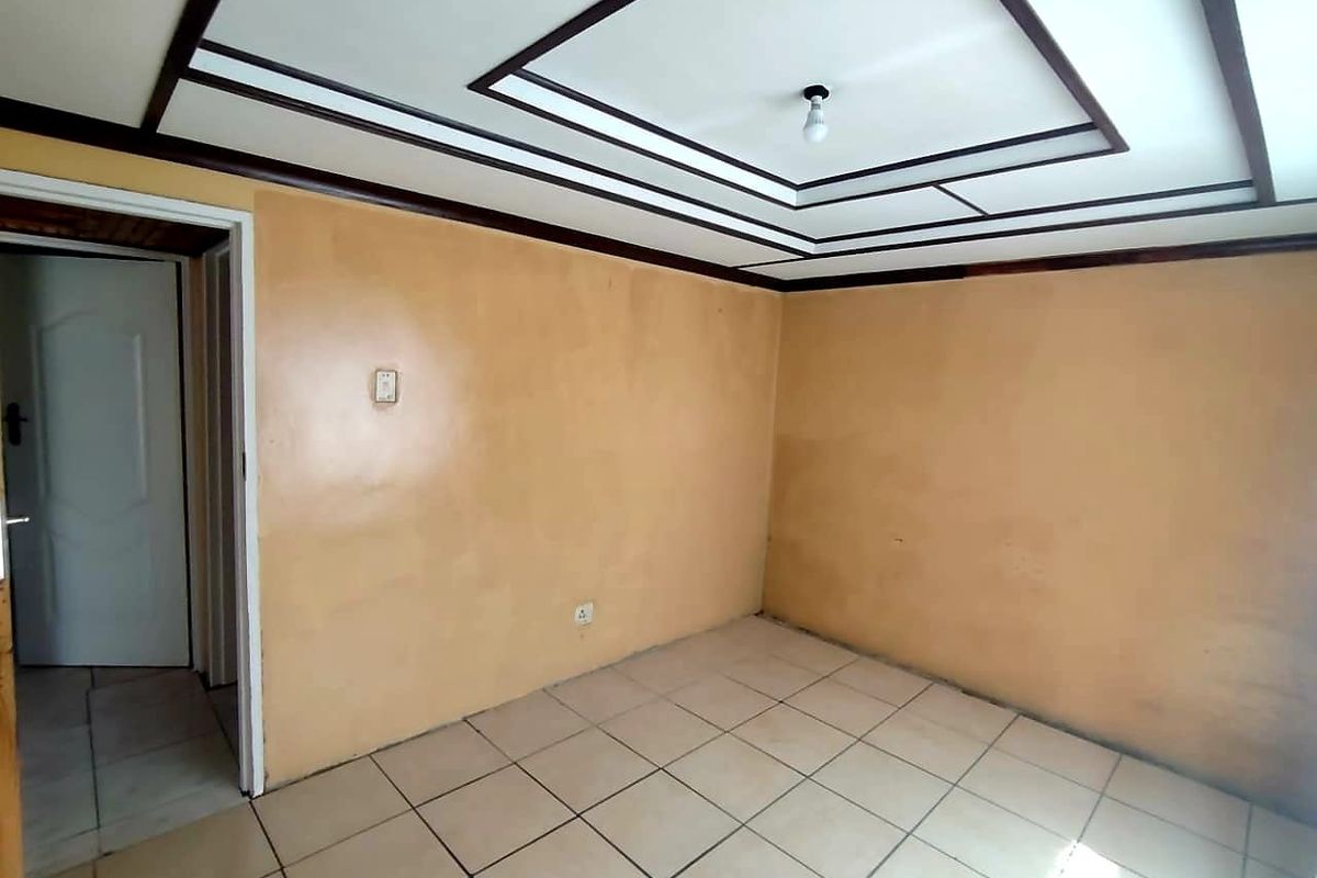 An empty bedroom featuring tiled flooring and a decorative tray ceiling, requiring cosmetic updates to the wall finishes.