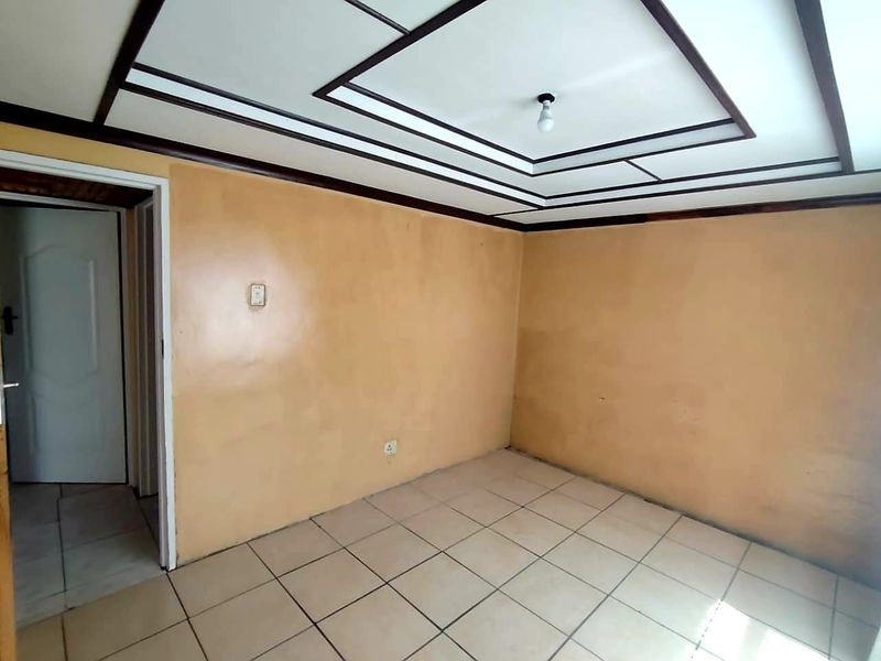 An empty bedroom featuring tiled flooring and a decorative tray ceiling, requiring cosmetic updates to the wall finishes.